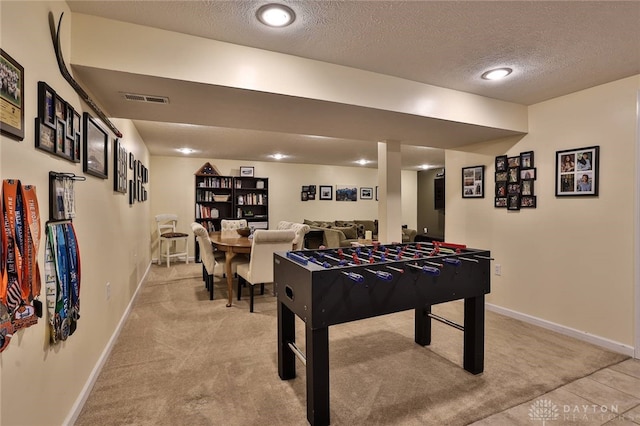 recreation room featuring visible vents, baseboards, a textured ceiling, and light colored carpet