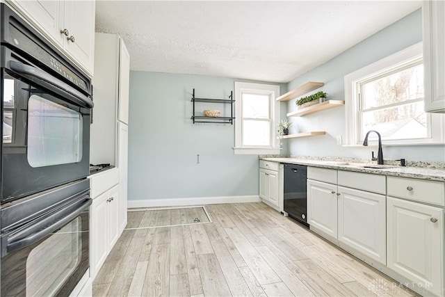 kitchen with baseboards, light wood-type flooring, white cabinets, a sink, and black appliances