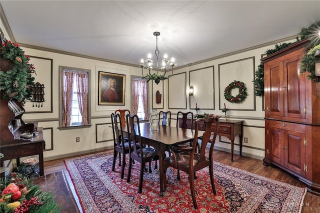 dining room with a notable chandelier, crown molding, a decorative wall, baseboards, and wood finished floors