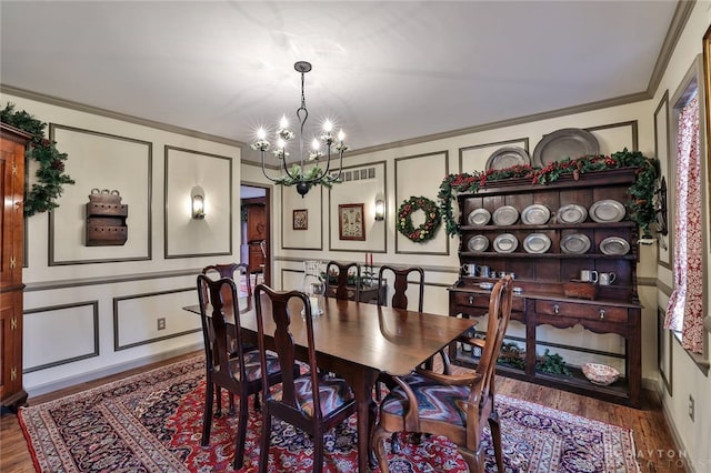 dining room with wood finished floors, an inviting chandelier, crown molding, and a decorative wall