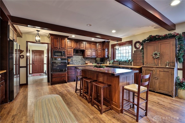 kitchen with beamed ceiling, built in microwave, a kitchen bar, backsplash, and black oven