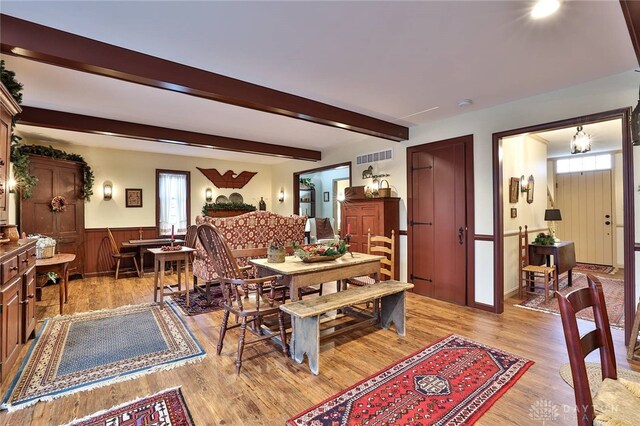 dining space featuring visible vents, a wainscoted wall, light wood-style flooring, and beamed ceiling