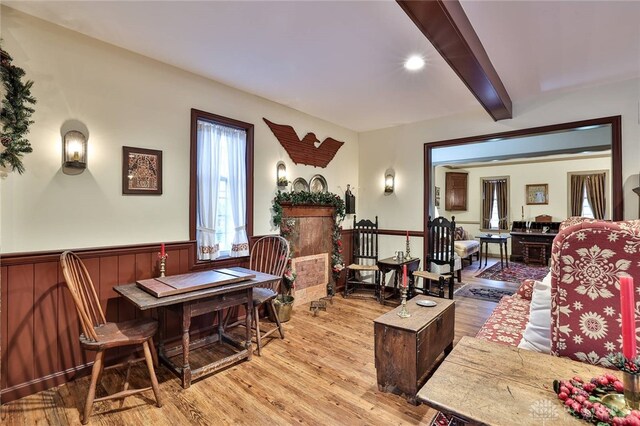 living room featuring beamed ceiling, wainscoting, and wood finished floors