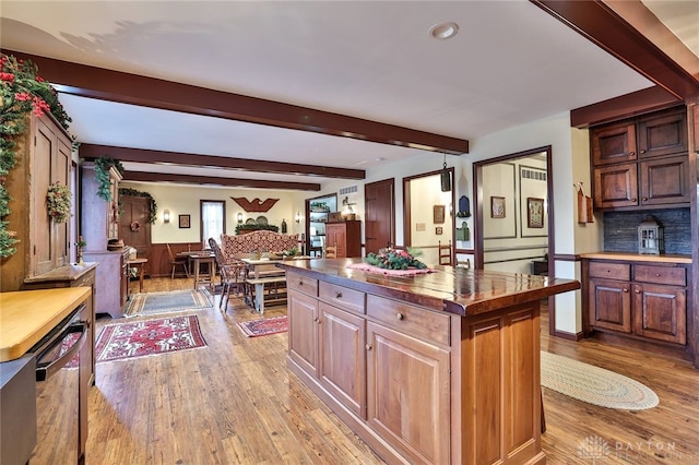 kitchen featuring beamed ceiling, light wood finished floors, a center island, a wainscoted wall, and butcher block counters