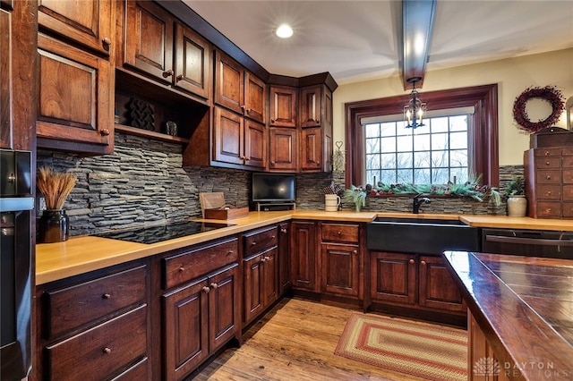 kitchen featuring light wood finished floors, a sink, tasteful backsplash, black appliances, and butcher block counters