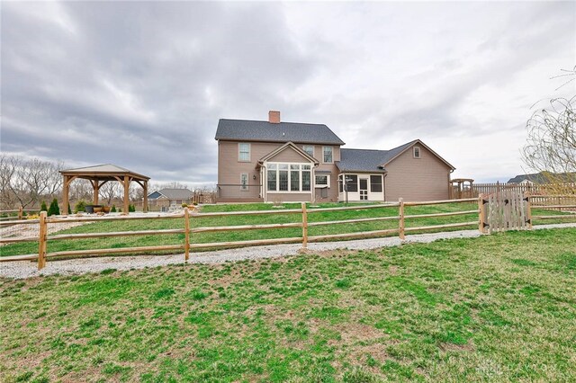 view of front of home with a front lawn, a gazebo, a fenced backyard, and a chimney
