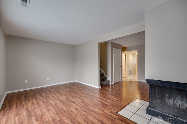 unfurnished living room featuring stairway, wood finished floors, visible vents, and baseboards