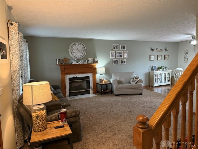 carpeted living area featuring a textured ceiling, ceiling fan, and a premium fireplace