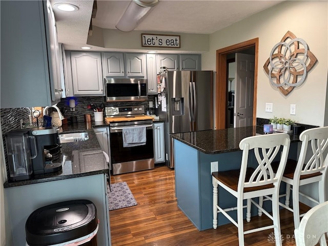 kitchen with a peninsula, dark wood-style flooring, a sink, appliances with stainless steel finishes, and a kitchen breakfast bar