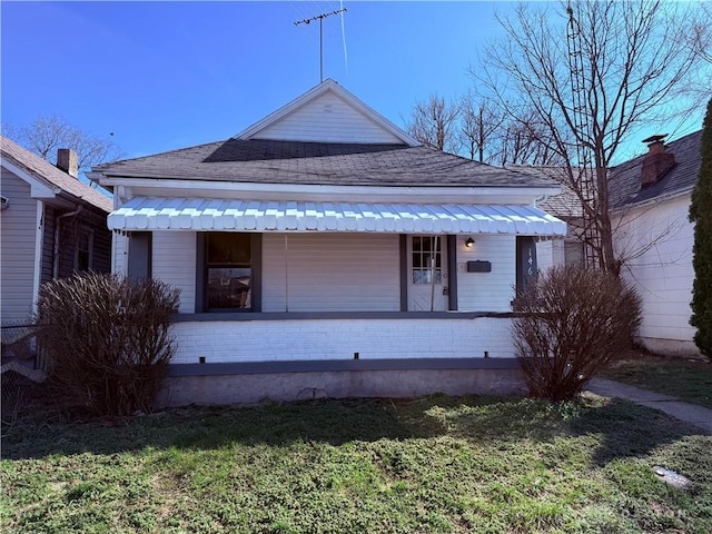 bungalow-style home with brick siding, a porch, a front yard, and a shingled roof