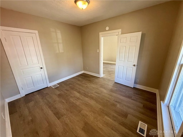 unfurnished bedroom with dark wood finished floors, baseboards, and visible vents