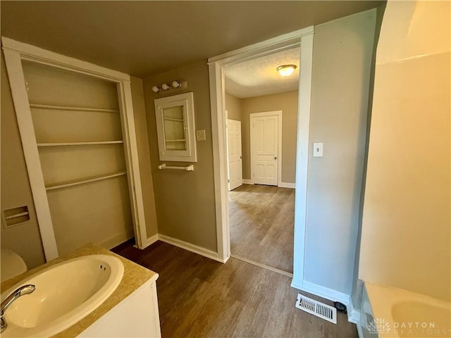 full bathroom featuring wood finished floors, baseboards, visible vents, a sink, and a textured ceiling