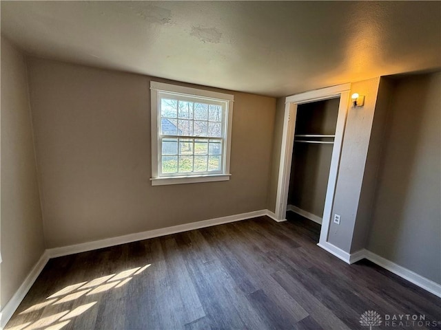 unfurnished bedroom with a closet, baseboards, and dark wood-type flooring