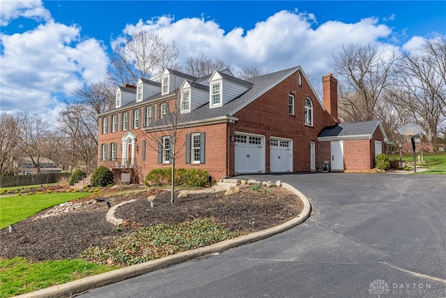view of front of house with driveway, a chimney, brick siding, and a garage