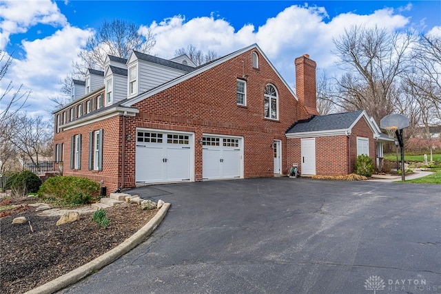 view of home's exterior with a chimney, brick siding, and aphalt driveway