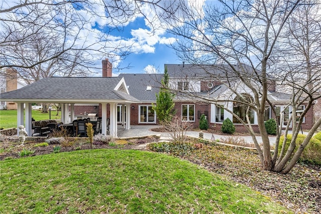 rear view of property featuring a patio, a yard, a chimney, and brick siding