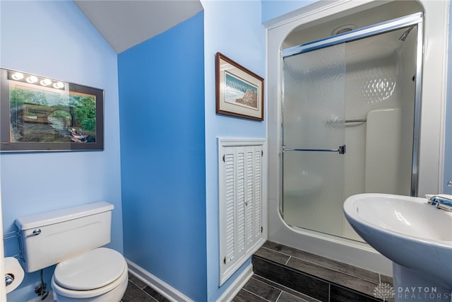 full bath featuring a sink, a stall shower, baseboards, toilet, and vaulted ceiling