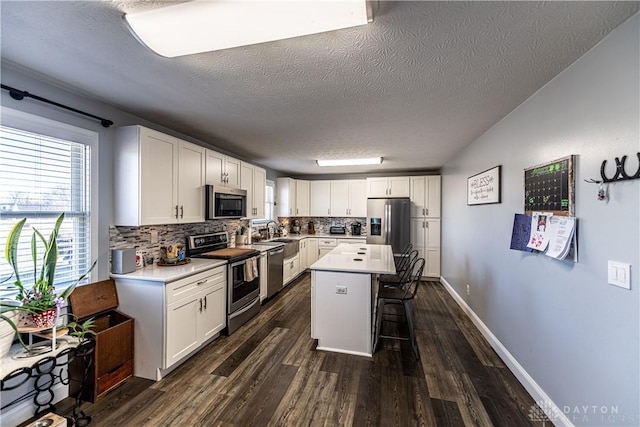 kitchen featuring decorative backsplash, a breakfast bar area, appliances with stainless steel finishes, white cabinetry, and a textured ceiling