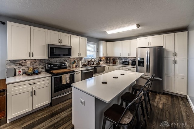 kitchen featuring dark wood finished floors, stainless steel appliances, a kitchen bar, a sink, and a textured ceiling