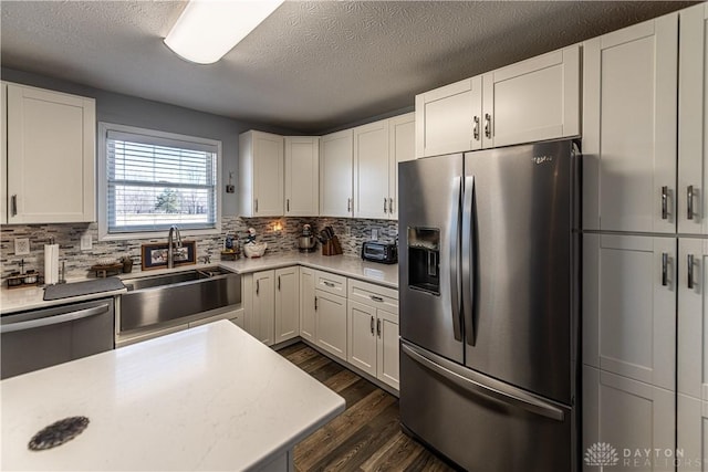 kitchen featuring a textured ceiling, a sink, stainless steel appliances, light countertops, and dark wood finished floors