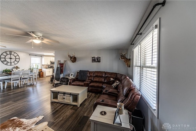 living room with a textured ceiling, ceiling fan, and dark wood-style floors