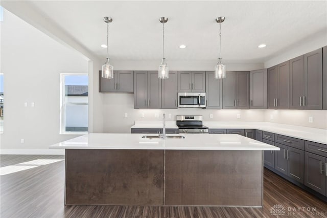 kitchen with light countertops, dark wood finished floors, appliances with stainless steel finishes, a sink, and an island with sink
