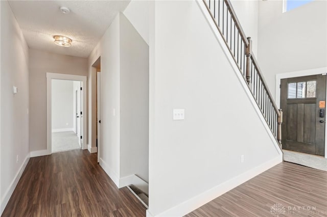 foyer entrance with baseboards, wood finished floors, stairway, and a textured ceiling
