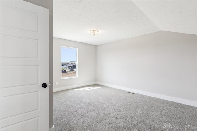 carpeted spare room featuring visible vents, baseboards, vaulted ceiling, and a textured ceiling