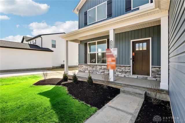 entrance to property with a lawn, stone siding, a porch, and board and batten siding