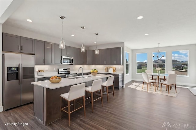 kitchen with light countertops, a sink, a kitchen breakfast bar, appliances with stainless steel finishes, and a center island with sink