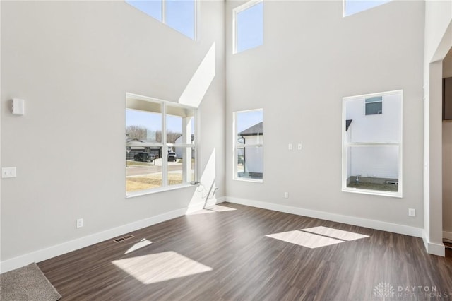 unfurnished living room with baseboards, dark wood-style floors, and plenty of natural light