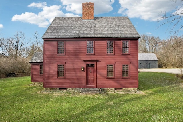 rear view of property featuring a chimney, a shingled roof, a yard, and an outbuilding