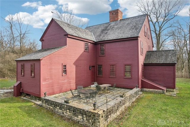 rear view of property with a lawn, a chimney, a patio, and roof with shingles