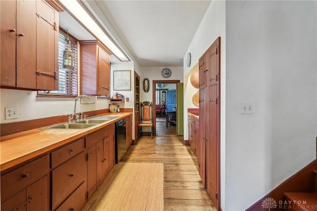 kitchen with black dishwasher, light wood finished floors, light countertops, and a sink
