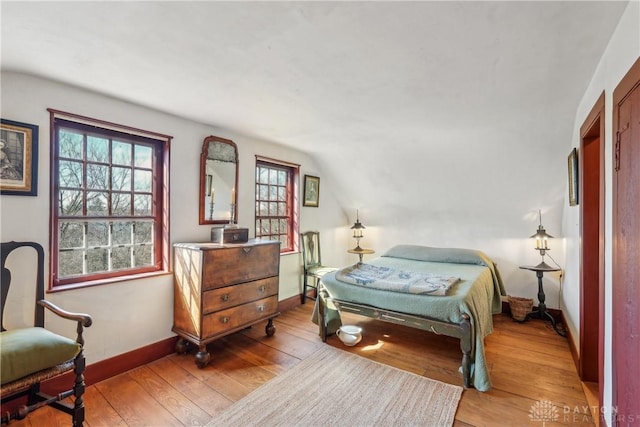 bedroom with baseboards, lofted ceiling, and hardwood / wood-style flooring