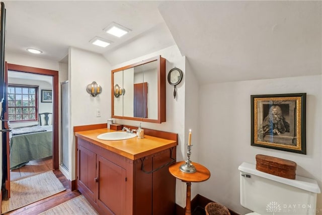 bathroom featuring wood finished floors, toilet, vanity, a shower with door, and ensuite bath