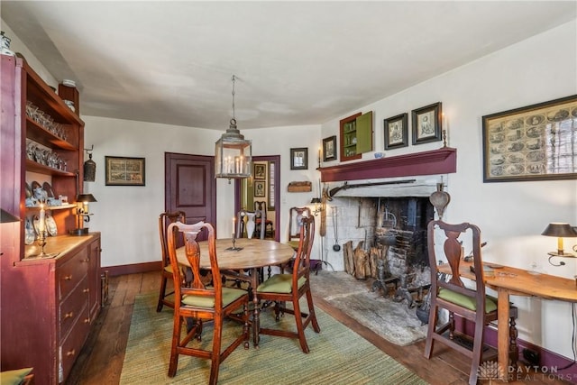 dining space with baseboards, dark wood-style floors, and a fireplace with raised hearth