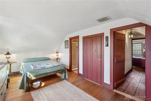 bedroom with visible vents, lofted ceiling, and hardwood / wood-style flooring