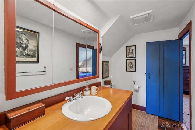 bathroom featuring visible vents, baseboards, wood finished floors, vanity, and vaulted ceiling