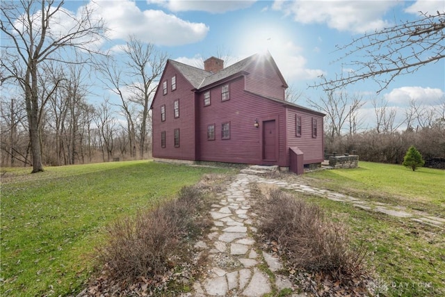 view of side of property with driveway, a chimney, and a lawn
