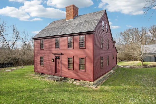rear view of property featuring a lawn, a chimney, and a shingled roof
