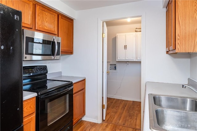kitchen featuring light countertops, a sink, light wood-style flooring, black appliances, and brown cabinetry