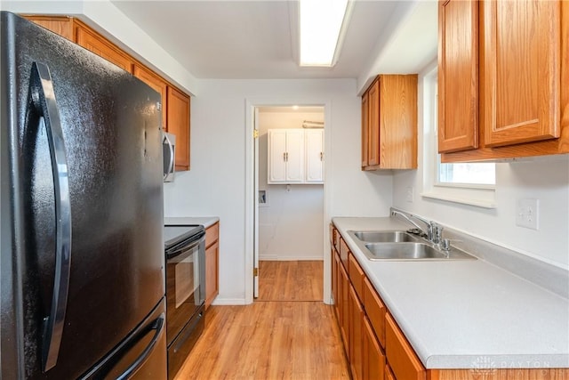 kitchen featuring light countertops, a sink, light wood-style floors, black appliances, and brown cabinets