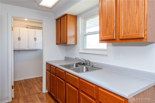 kitchen with light countertops, a sink, brown cabinetry, and light wood-style flooring