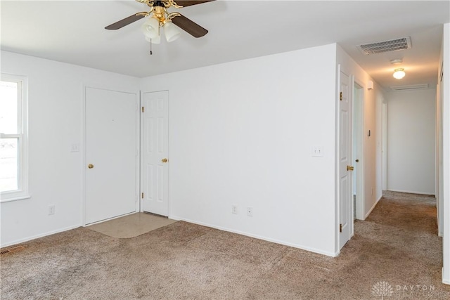 carpeted empty room featuring ceiling fan, visible vents, and plenty of natural light