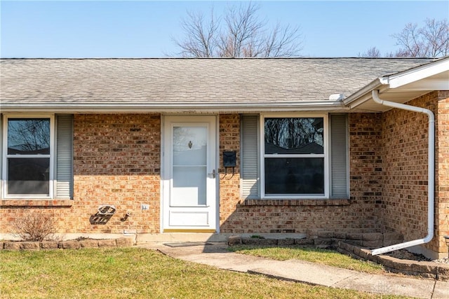 view of exterior entry with brick siding and roof with shingles