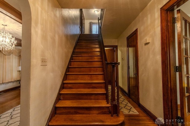 stairway with baseboards, wood finished floors, a textured wall, and a chandelier