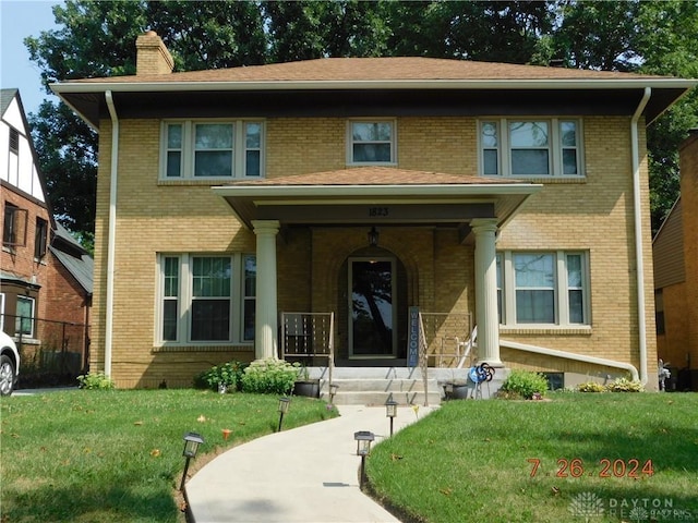 american foursquare style home featuring a front lawn, a chimney, and brick siding