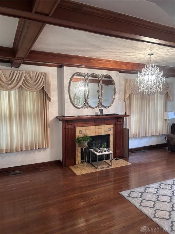 unfurnished living room with a tiled fireplace, beam ceiling, a chandelier, wood finished floors, and baseboards