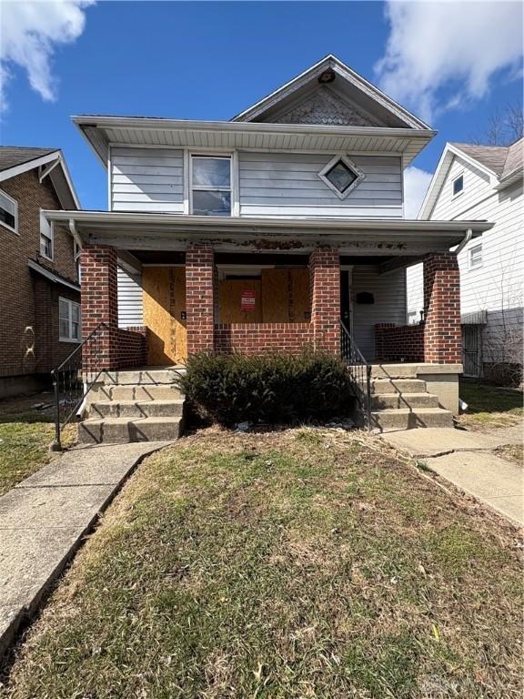 traditional home with covered porch, a front lawn, and brick siding
